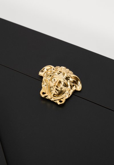 Melna virsma ar izteiktu greznu zelta furnitūru ar sejas dizainu. Tekstūra ir gluda ar spoguļotu virsmu.