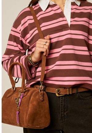 Woman wearing a pink and brown striped shirt, holding a brown suede handbag with heart and rope keychains.