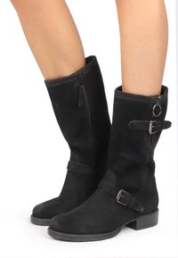 Bottes noires en daim montantes avec fermeture éclair sur le côté, accent de boucle et un talon bloc bas pour la stabilité. Texture lisse avec un minimum de détails.