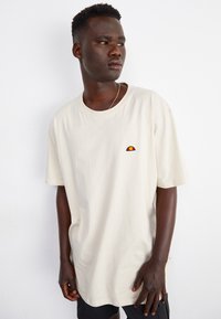 Light beige cotton t-shirt with a round neckline, short sleeves, and a small multicolored logo on the chest. Smooth texture.