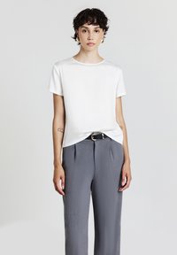 Blusa bianca a maniche corte con una texture liscia, scollatura rotonda e vestibilità morbida, abbinata a pantaloni grigi larghi e una cintura nera.