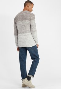 Gebreide trui in grijs en witte strepen, met een relaxte pasvorm. Gepaard met blauwe denim jeans en crèmekleurige sneakers.