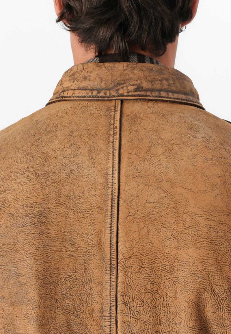 Giacca di pelle marrone invecchiata con dettagli testurizzati, cuciture visibili lungo il colletto e sul retro, che mostrano un aspetto robusto.