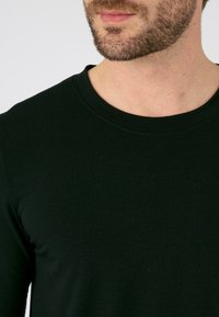 Zwarte langeman shirt gemaakt van zacht, glad materiaal met een ronde hals. Kenmerkt zich door een getailleerde silhoeet en minimale naden voor een strakke uitstraling.