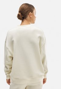 Sudadera de color beige claro, de corte oversized, con cuello redondo, hombros caídos y puños de canalé. Material de algodón suave con una textura lisa.