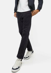 Marineblauwe corduroybroek met een slim fit, met zijzakken. Gecombineerd met witte en marineblauwe sneakers op een effen achtergrond.