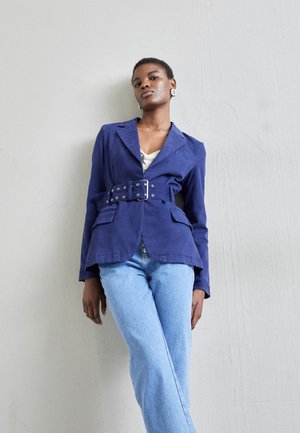 Námornícka modrá sako s opaskom vyrobené z bavlny, s prednými vreckami a prispôsobeným dizajnom. V kombinácii so svetlomodrými nohavicami s rovnými nohavicami.