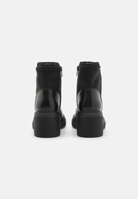 Botas negras hasta el tobillo que combinan cuero liso y tela texturizada, con cierre de cremallera y un tacón grueso acanalado.