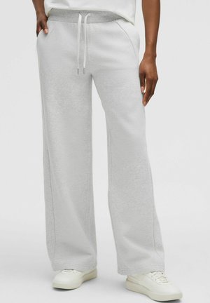 Pantaloni de trening gri deschis, cu o croială lejeră, talie cu șnur, buzunare laterale și textură moale, asortați cu adidași albi.