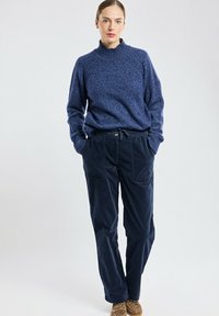 Pull en maille bleu marine à col haut, associé à un pantalon en velours côtelé bleu marine foncé avec deux poches avant et une taille à cordon.