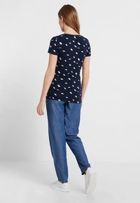 Navy t-shirt with short sleeves, featuring a scattered white leaf pattern. Paired with loose-fitting blue denim pants and white sneakers.