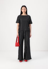 Čiernobiely pruhovaný outfit so štvorcovým výstrihom, krátkymi rukávmi a širokými nohavicami. Doplněný červenou kabelkou na rameno a topánkami.