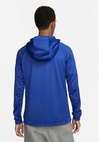 Blå letvægts hoodie med en afslappet pasform og snørre. Har en glat tekstur og lange ærmer, vist fra ryggen med grå bukser.