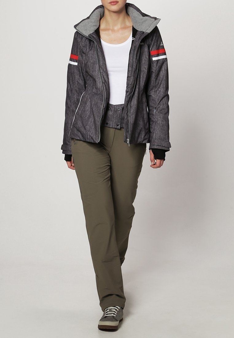 Giacca grigia strutturata con cappuccio grigio, strisce rosse e bianche sulle maniche, abbinata a pantaloni verde oliva e sneaker grigie.