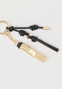 Μπρελόκ από χρυσό μέταλλο με σωληνωτό σχέδιο, που φέρει ένα εξέχον λογότυπο 'G', προσαρτημένο σε μαύρα δερμάτινα κορδόνια με κόμπους.