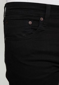 Vaqueros de mezclilla negra con una textura suave, que cuentan con herrajes en tono bronce, costuras en contraste y un diseño de bolsillo frontal.