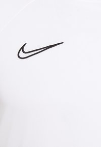 Valkoinen urheilupaita mustalla Nike Swoosh -logolla. Ominaisuuksiin kuuluvat sileä pinta ja lyhyet hihat, valmistettu hengittävästä kankaasta mukavuutta varten.