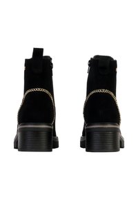 Bottines en suède noir avec fermeture éclair, ornées d'une chaîne en or décorative et d'un talon bloc texturé. Texture lisse dans l'ensemble.