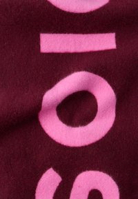 Sötét bordó szövet puha textúrával, nagy rózsaszín absztrakt formákkal és betűkkel, beleértve egy feltűnő kört és vonalakat.