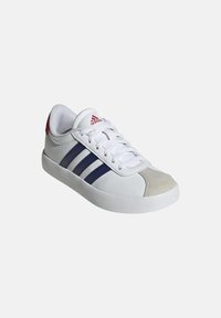 Sneaker bianca con righe navy, punta in suede grigia e dettagli rossi sul tallone. Presenta lacci bianchi e una suola in gomma.