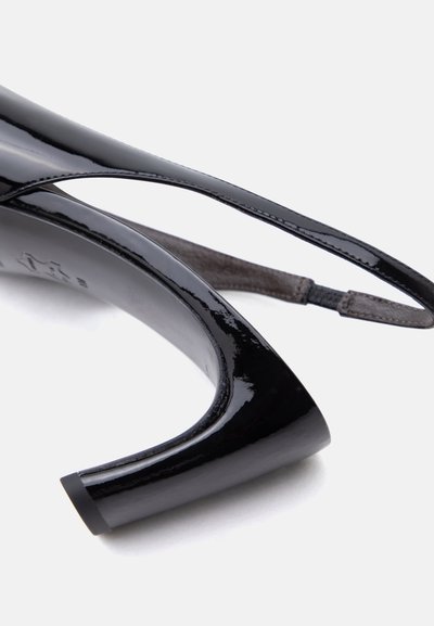 Μαύρο γυαλιστερό δερμάτινο ψηλοτάκουνο με καμπυλωτό χοντρό τακούνι και λεπτό ρυθμιζόμενο λουράκι στον αστράγαλο σε λευκό φόντο.