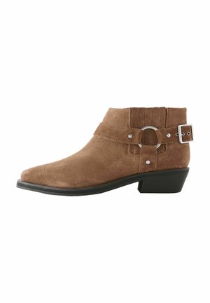 Bottine en daim marron avec un bout pointu, une boucle décorative avec anneau et un talon bas. Tige texturée avec coutures verticales.