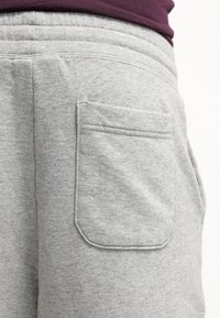 Pantalones de chándal grises con una textura suave, que cuentan con un bolsillo trasero de forma rectangular y detalles de costura. Cintura elástica visible en la parte superior.