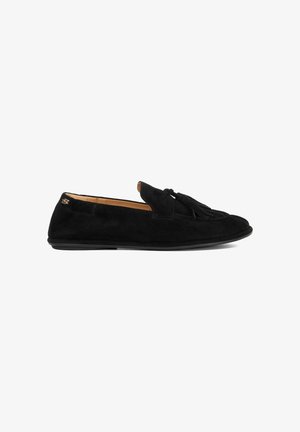 Zwarte nubuck instappers met een platte zool, voorzien van een voorste kwastdetail en leren voering. Minimalistisch ontwerp zonder zichtbare hardware.