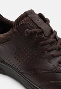 Braune Leder-Sneaker mit textilen Akzenten, Perforationen an der Seite, runden Schnürsenkeln und einem Logo-Patch auf der Zunge. Strukturiertes Gummisohle.