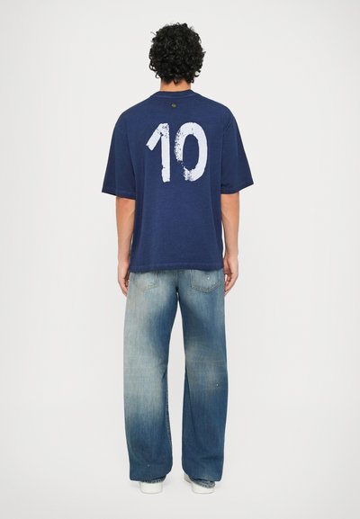 Mørkeblå oversized t-skjorte med et stort hvitt "10" trykket på ryggen, kombinert med lyseblå denim straight-leg jeans.