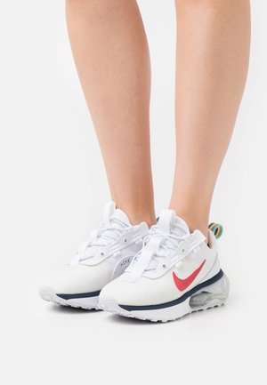 Legs wearing white Nike sneakers with red swoosh, transparent air cushion soles, and multicolor pull tabs against a plain white background.