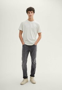 Light gray short-sleeve t-shirt, dark gray jeans, and cream sneakers. The t-shirt has a subtle logo, with a relaxed fit and soft texture.