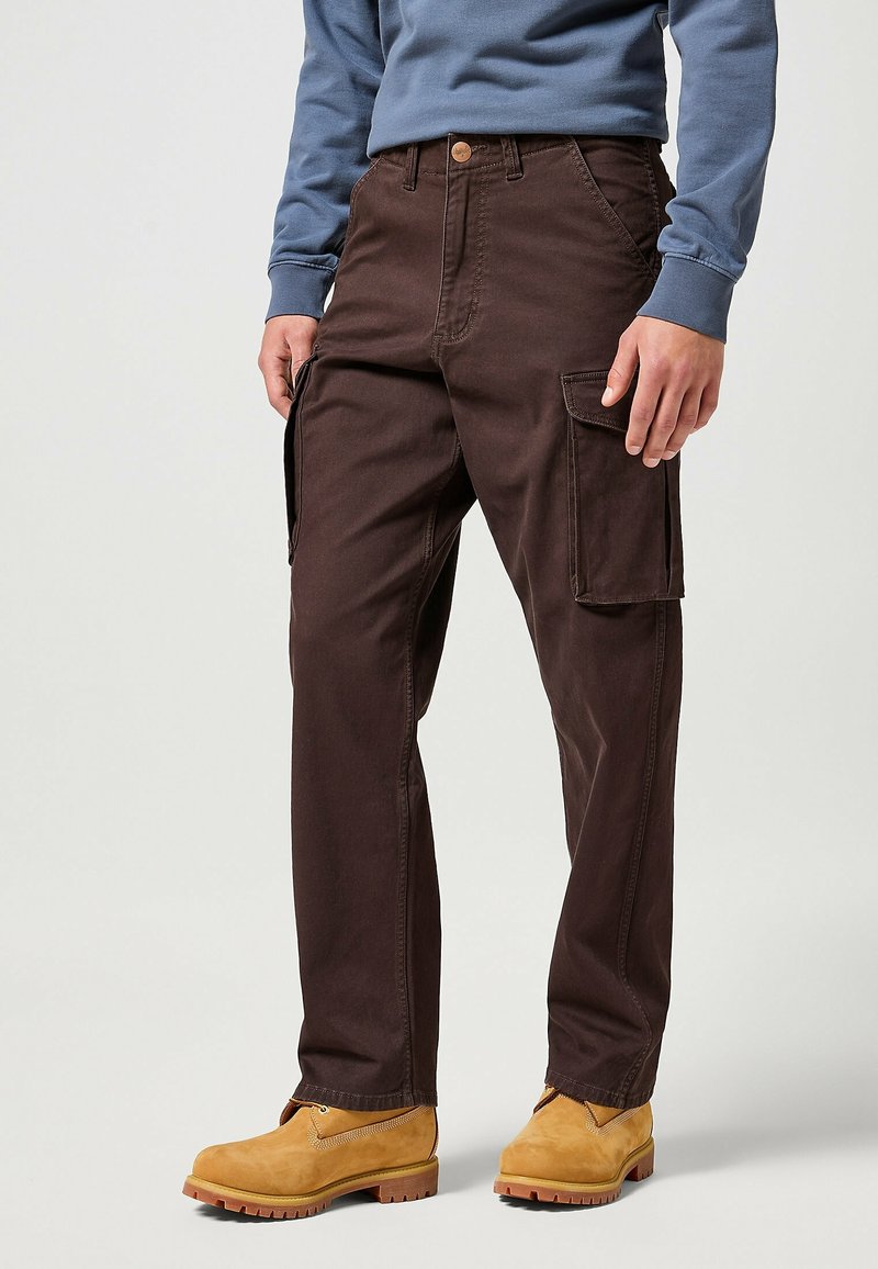 Bruna cargobyxor med en avslappnad passform, som har sidofickor, slitstarkt tyg och förstärkt sömnad, tillsammans med gula arbetsskor.