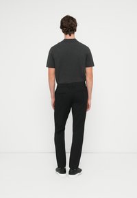 Ciemnoszara koszulka polo z krótkim rękawem w zestawie z czarnymi dopasowanymi spodniami i czarnymi sneakersami. Prosty design, gładka tekstura i dopasowany krój.