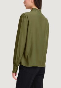 Blusa verde oliva a maniche lunghe con scollo arricciato, caratterizzata da spalle arricciate e polsini con bottoni, realizzata in tessuto leggero e liscio.