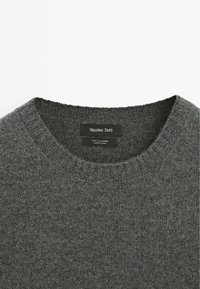 Dunkelgrauer Kaschmirpullover mit einem gerippten Rundhalsausschnitt, der eine weiche Textur und ein minimalistisches Design aufweist. Das Etikett trägt die Aufschrift "Massimo Dutti."