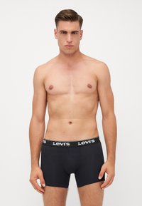 Boxer in cotone neri con un design aderente, tessuto morbido e una vita con marchio a contrasto. Il modello è in piedi con le braccia rilassate ai lati.