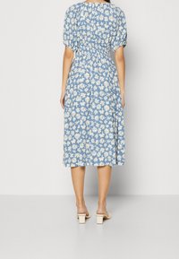 Blå blommig midi-klänning med puffärmar, samlad midja, vitt prästkragmönster och mjukt tyg. Klacken sandaler fulländar looken.