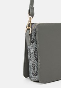 La borsa sintetica grigia presenta un pannello in stampa serpente, una chiusura a zip e una tracolla staccabile. Gli accenti in oro migliorano il design.