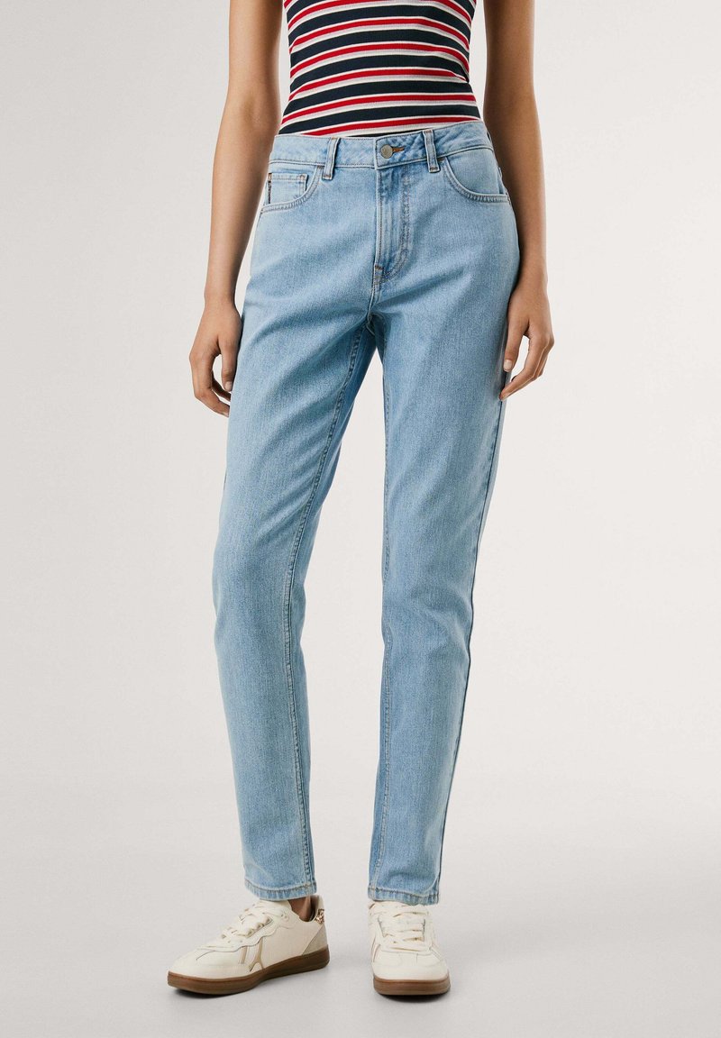 Vaqueros de denim azul claro con cintura alta, corte recto, bolsillos frontales y un sutil patrón desgastado, combinados con zapatillas blancas.