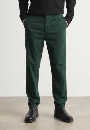 Green cotton chinos with a straight fit, featuring front pockets and a smooth texture, paired with black ankle boots.
