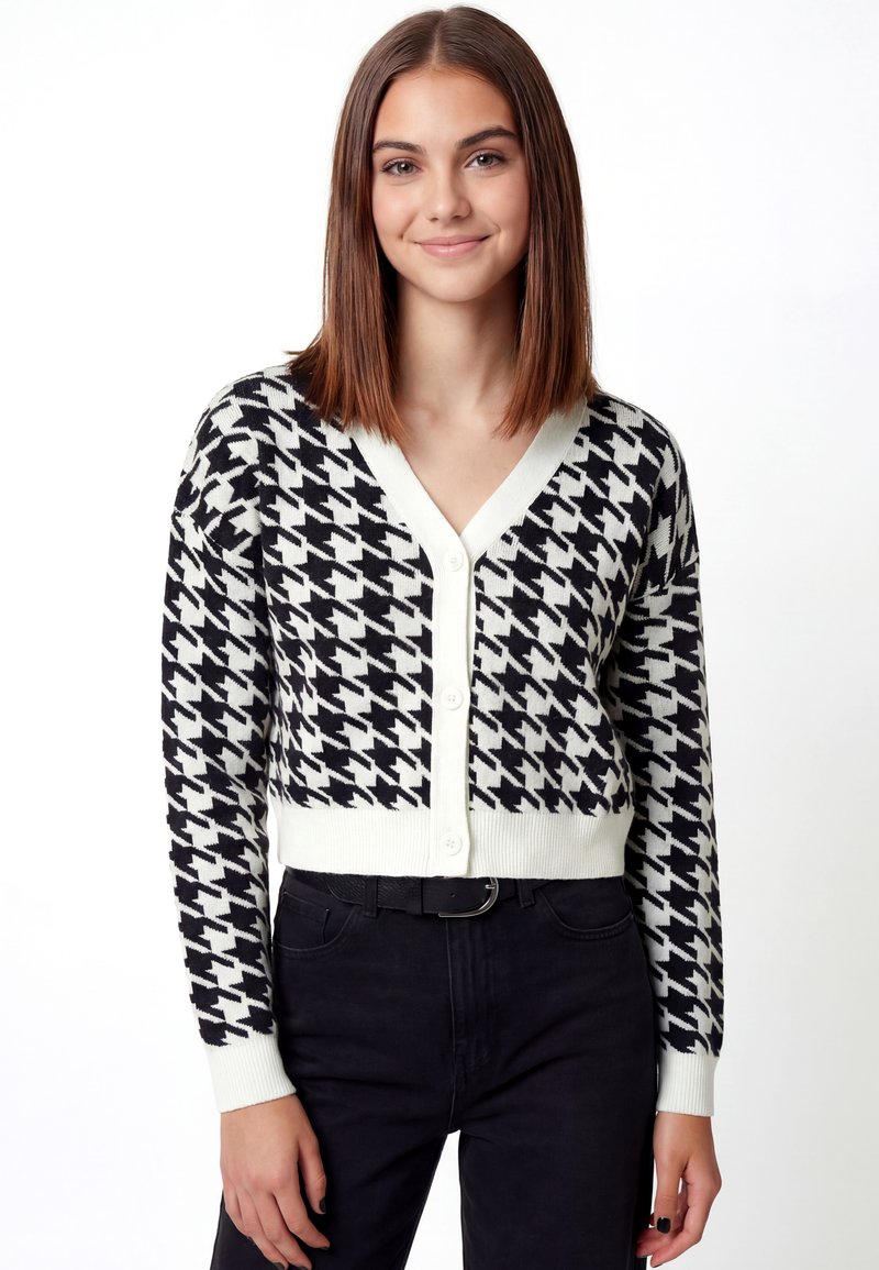 Zwart-witte vest met pied-de-poule patroon, V-hals, knopen aan de voorkant en geribbelde boorden, gecombineerd met een zwarte broek.