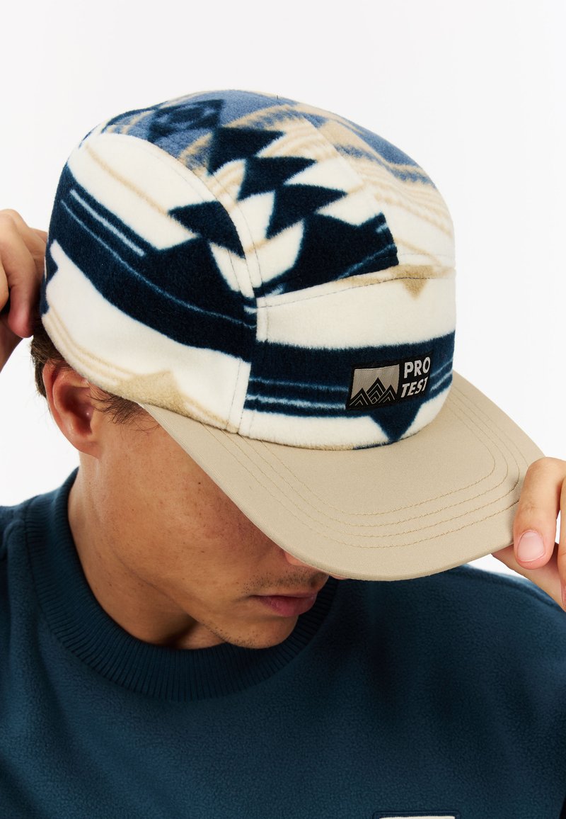 Multi-colored cap with a fleece patterned top in navy and beige, featuring a flat brim and a black logo tag on the front.