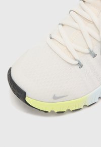 Zapatilla de running ligera con empeine de malla blanca, cordones grises y suela exterior texturizada en negro y amarillo; presenta un detalle sutil de la marca.