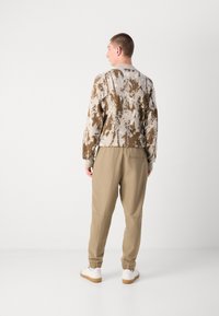 Brun mönstrad tröja med en texturerad yta, i kombination med ljusbeige, avsmalnande joggers med elastiska muddar och en bakficka.