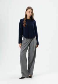 Pull en maille bleu marine associé à un pantalon gris à jambes larges. Chaussures noires à bout pointu. Design simple avec une coupe décontractée et un minimum de détails.
