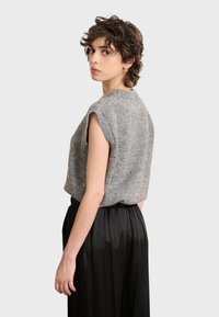 Graues, kurzärmeliges Strickoberteil mit rundem Ausschnitt, kombiniert mit schwarzen, hochgeschnittenen, gefalteten Hosen, glatte Textur sichtbar.