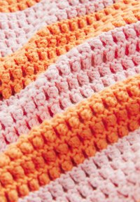 Gros plan d'un tissu tricoté texturé avec des larges rayures alternées en rose doux et orange vif.
