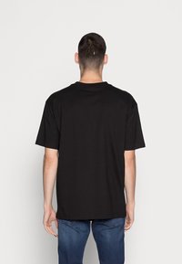 Černé tričko s krátkým rukávem a kulatým výstřihem, vyrobené z bavlny. Vyznačuje se volným střihem a jednotnou barvou bez vzorů nebo akcentů.