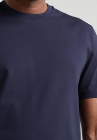 Granatowa koszulka z okrągłym dekoltem i krótkim rękawem. Wykonana z gładkiej, lekkiej tkaniny, o dopasowanym kroju i bez widocznych wzorów.